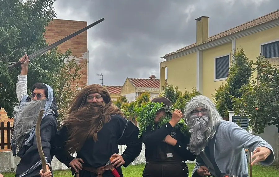 Four of our players outdoors in costume under a grey sky, one with a raised sword, two in long grey and brown wigs, one crowned with leaves