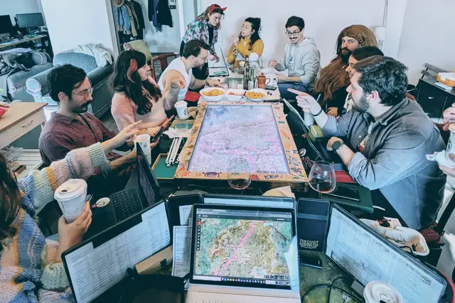 Our own table mid-session: a dozen people around a hand-drawn map, with dice, laptops and glasses between them